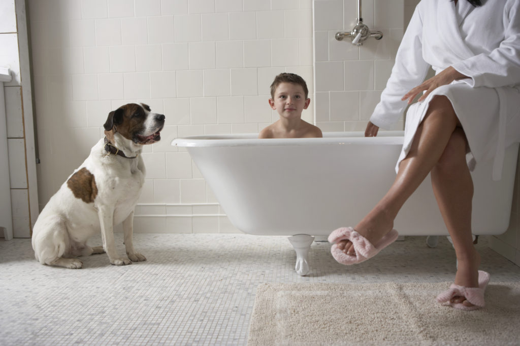 Mother sitting on side of tub with son (6-8) in bath tub and with dog